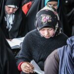 Group of Afghan girls in traditional attire focused on reading during a community event.